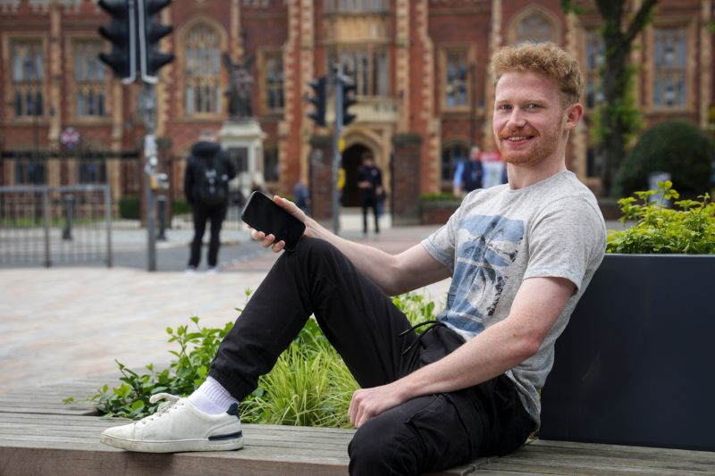 student looking at phone across from the main Queen's building